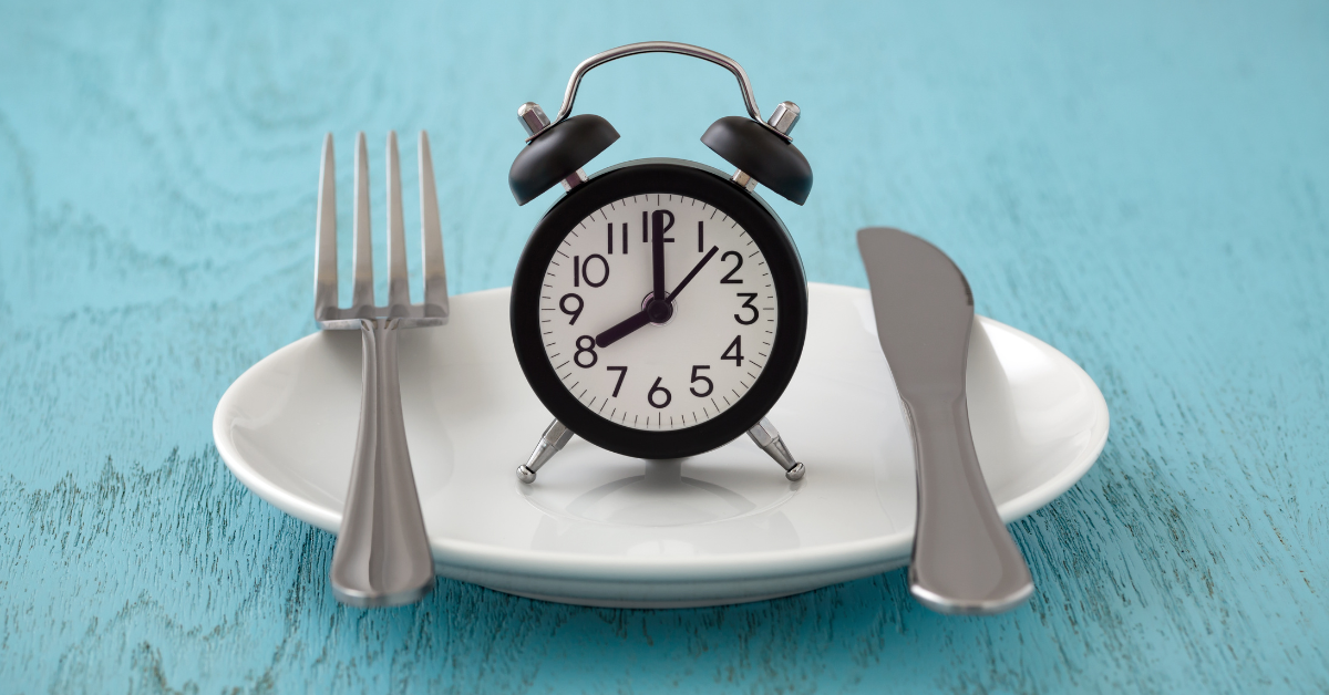 An alarm clock on a plate with a spoon and fork beside it.